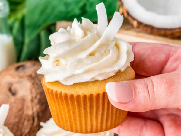 A hand holding a coconut cupcake with a green background.