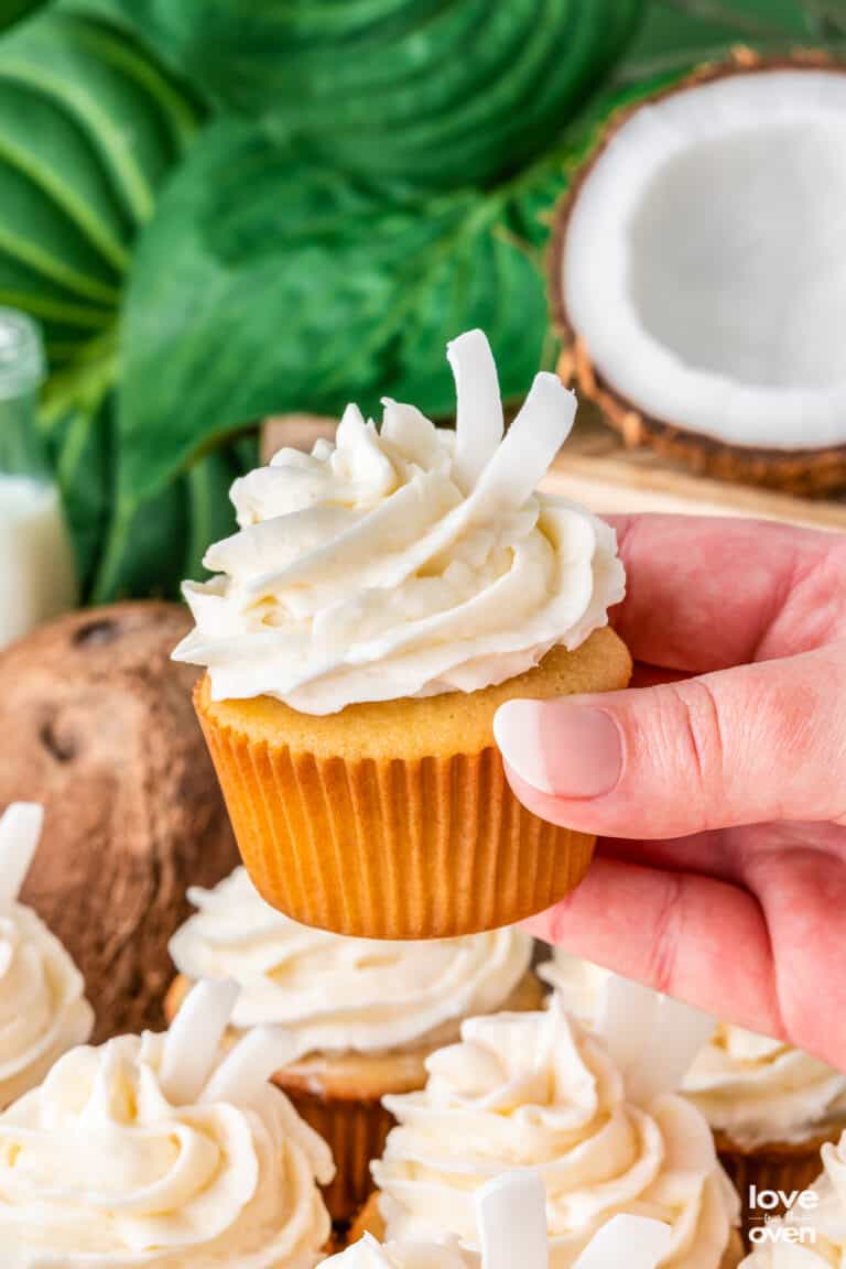 A hand holding a coconut cupcake with a green background.