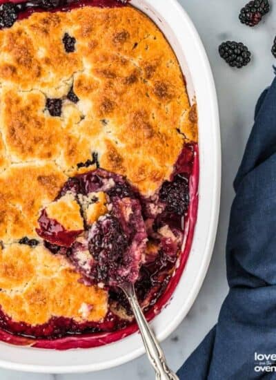 A spoon taking a serving of blackberry cobbler out of a baking dish.