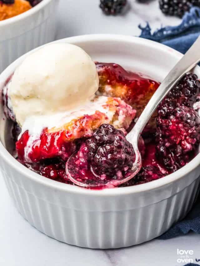 blackberry cobbler topped with ice cream in a ramekin with a spoon taking a bite out