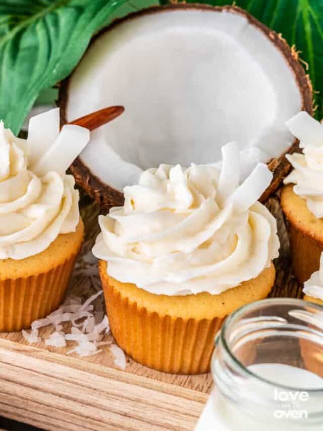 coconut cupcakes on a wooden stand next to a halved coconut