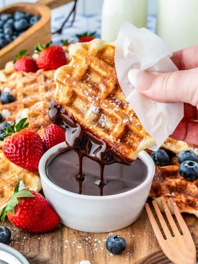 A liege waffle being dipped into chocolate sauce.