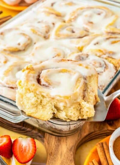 A cinnamon roll being taken out of a pan of cinnamon rolls.