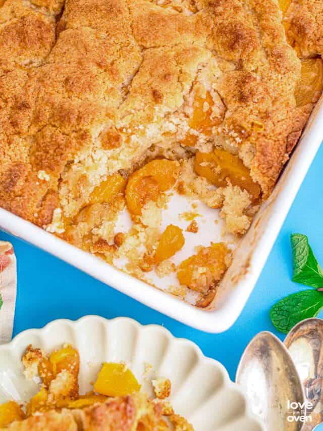 a baking dish of peach cobbler with a serving taken out of it