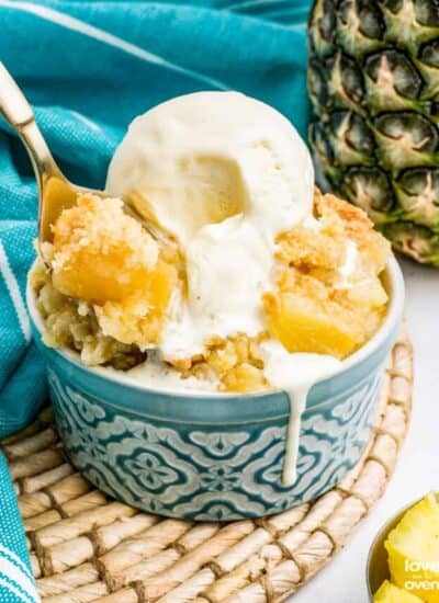 A pineapple dump cake in a blue bowl, topped with ice cream.