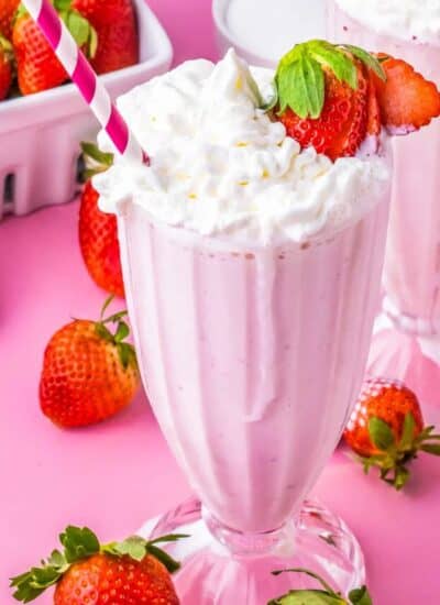 a strawberry milkshake with a strawberry on the edge of the glass and a pink and white straw