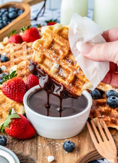 A liege waffle being dipped into chocolate sauce.
