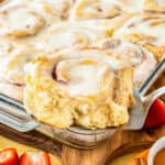 A cinnamon roll being taken out of a pan of cinnamon rolls.