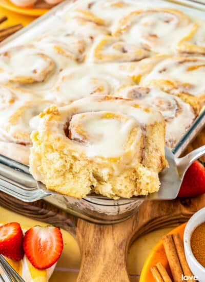 A cinnamon roll being taken out of a pan of cinnamon rolls.