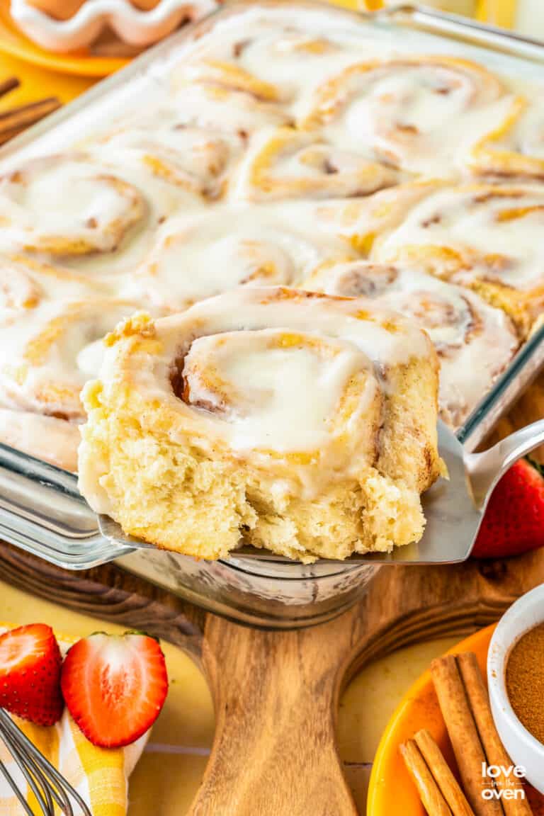 A cinnamon roll being taken out of a pan of cinnamon rolls.