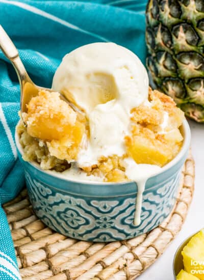 A pineapple dump cake in a blue bowl, topped with ice cream.