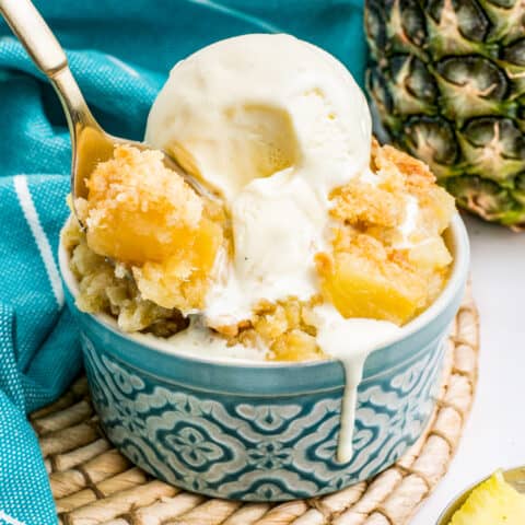 A pineapple dump cake in a blue bowl, topped with ice cream.