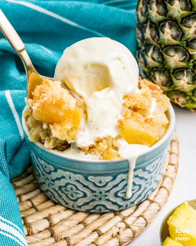 A pineapple dump cake in a blue bowl, topped with ice cream.