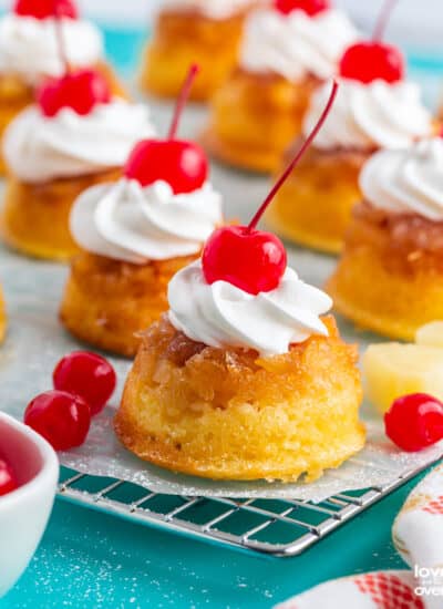 A batch of pineapple upside down cupcakes topped with whipped cream and cherries