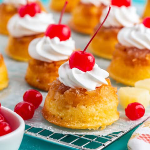 A batch of pineapple upside down cupcakes topped with whipped cream and cherries