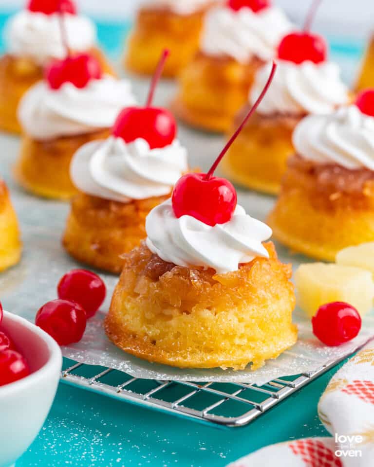 A batch of pineapple upside down cupcakes topped with whipped cream and cherries