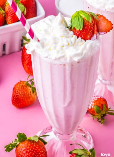 a strawberry milkshake with a strawberry on the edge of the glass and a pink and white straw