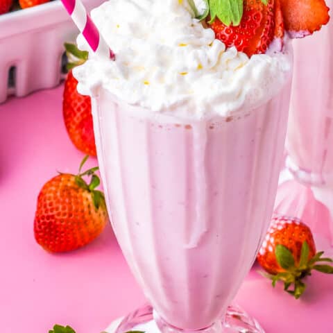 a strawberry milkshake with a strawberry on the edge of the glass and a pink and white straw