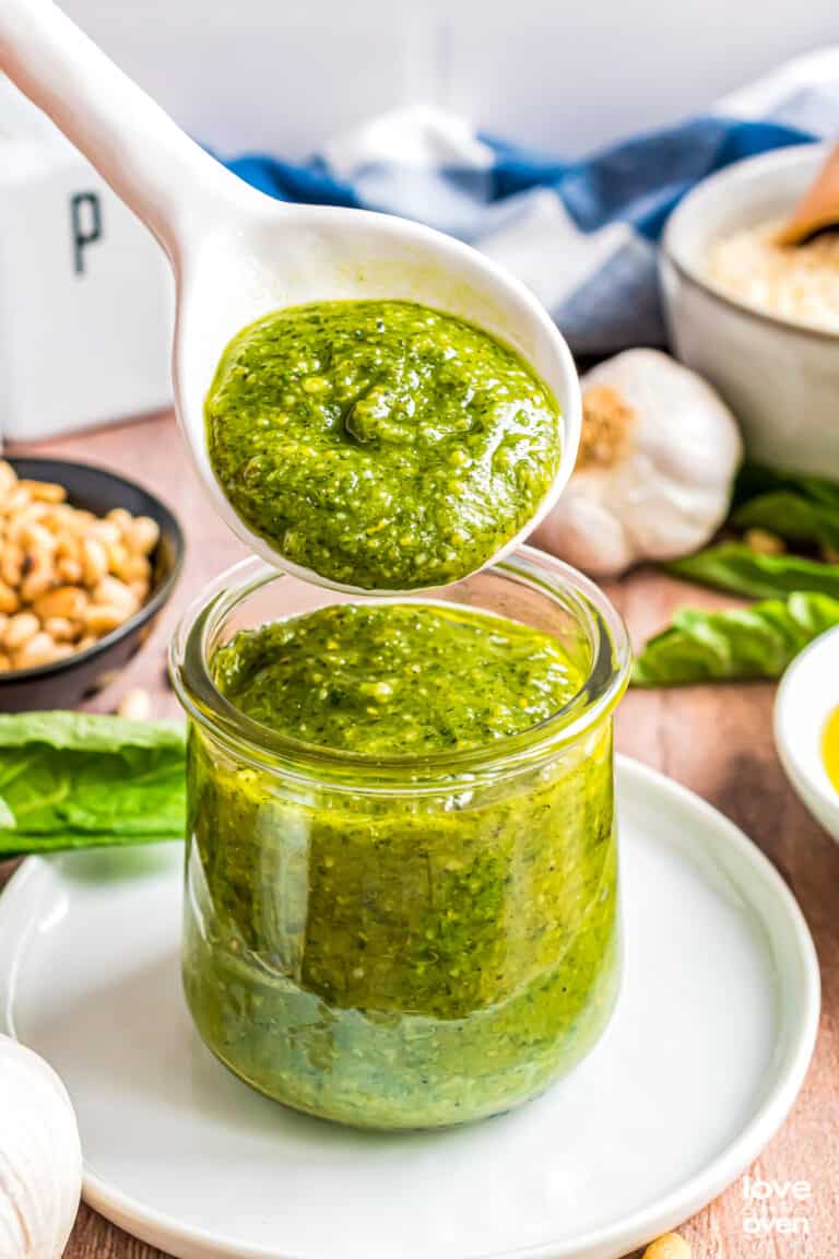 A spoon with a spoonful of homemade pesto sauce over a jar of pesto.