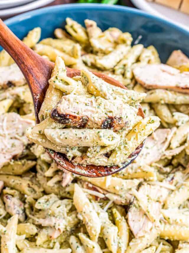 a wooden serving spoon picking up some pesto chicken pasta
