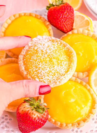 A hand grabbing one of many lemon tarts.