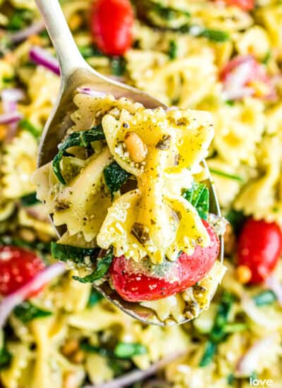 A close up of a spoon holding pesto pasta salad.