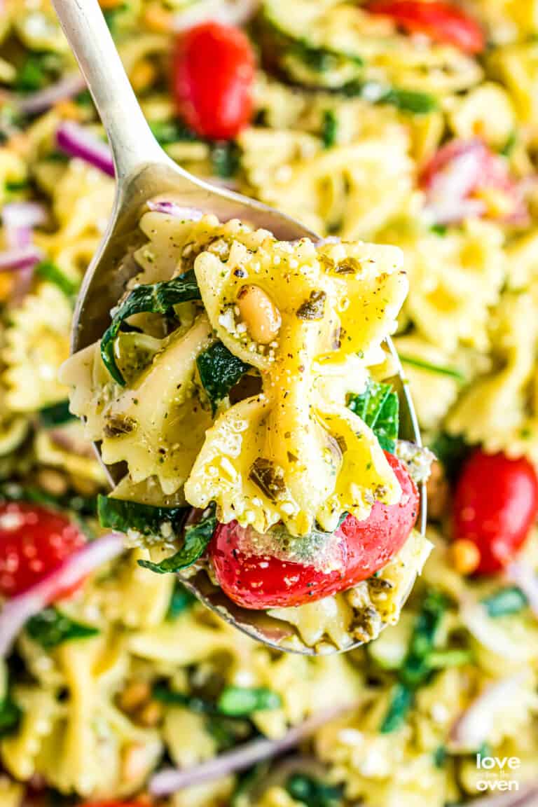 A close up of a spoon holding pesto pasta salad.