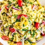 A spoon holding a serving of pesto pasta salad over a bowl full of pasta salad.