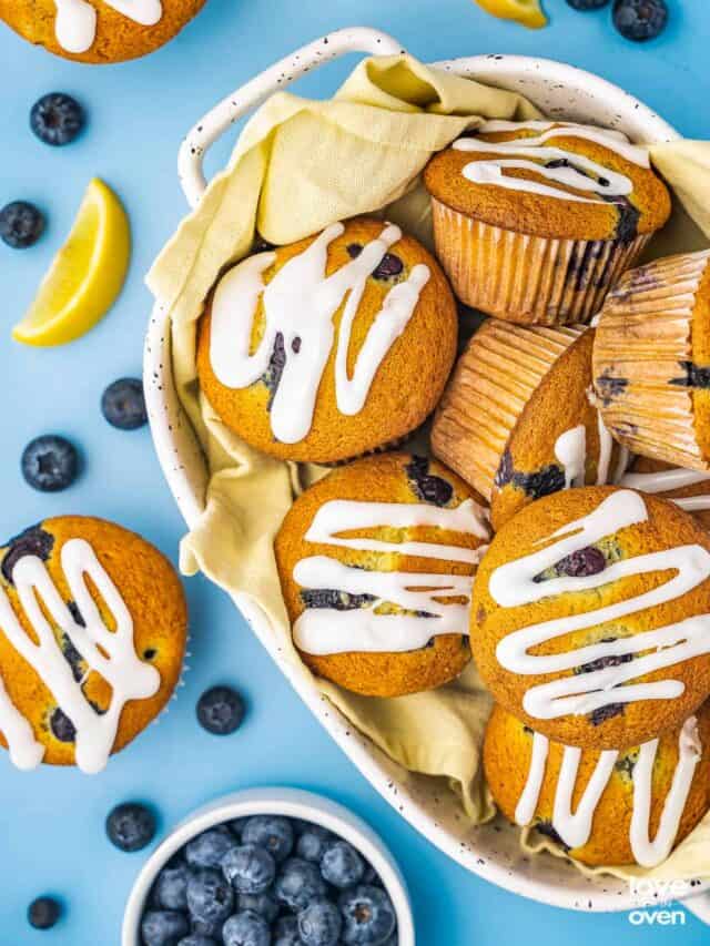 A bowl filled with lemon blueberry muffins with blueberries and lemon slices around it.