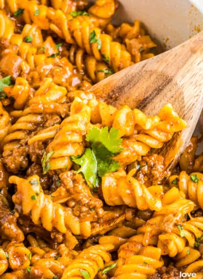 A wooden spoon grabbing a spoonful of enchilada pasta from a pan.