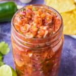 A jar of chunky homemade salsa on a purple background.