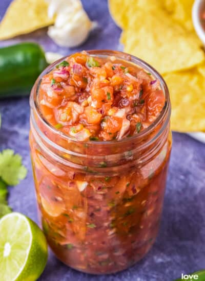 A jar of chunky homemade salsa on a purple background.