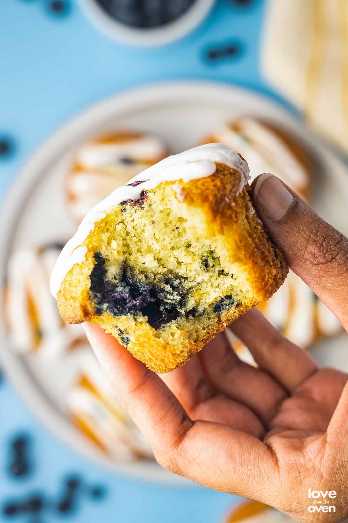 a hand holding a lemon blueberry muffin with a bite taken out of it