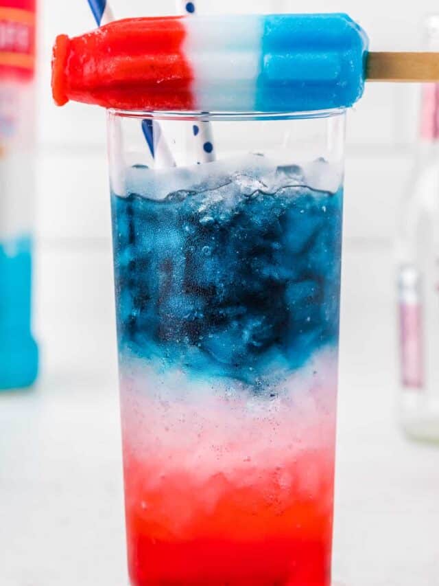 A bomb pop sitting on top of a glass of red white and blue cocktail