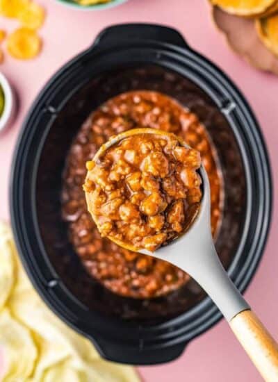 A crock pot full of sloppy joes with a spoon taking a serving out.