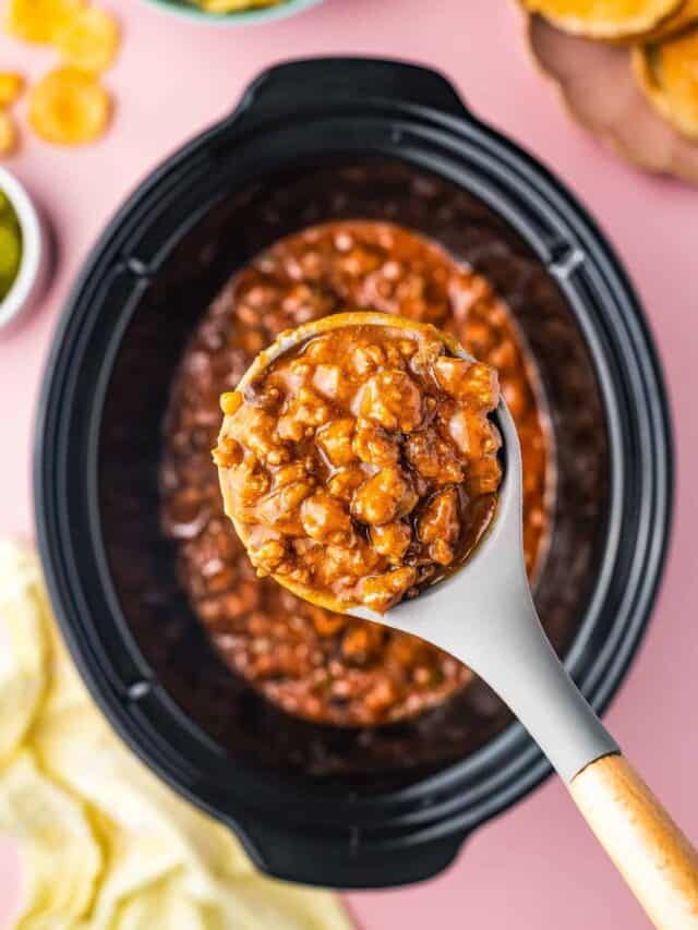 A crock pot full of sloppy joes with a spoon taking a serving out.