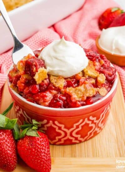 A spoon grabbing a portion of a strawberry dump cake topped with whipped cream.