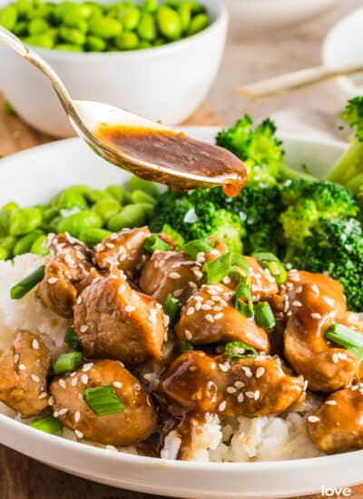 A spoon pouring teriyaki sauce over teriyaki chicken