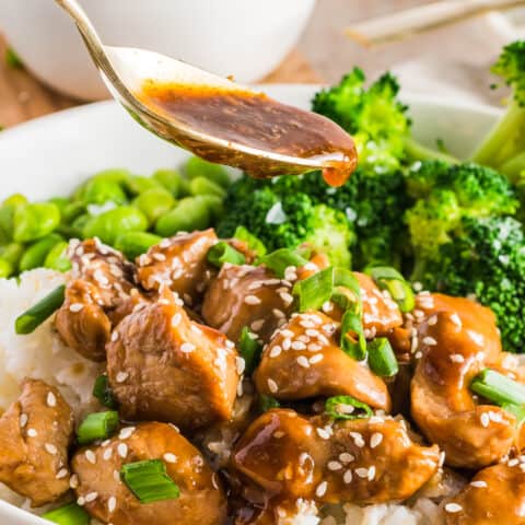 A spoon pouring teriyaki sauce over teriyaki chicken