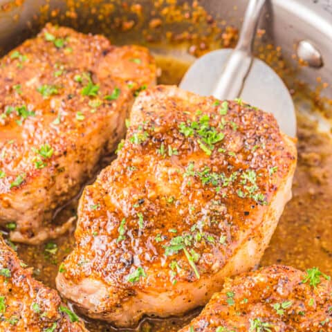 honey mustard pork chops on a skillet being flipped by a spatula