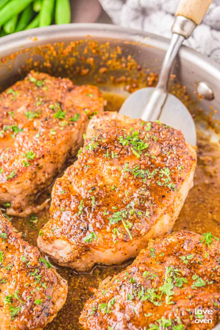 honey mustard pork chops on a skillet being flipped by a spatula