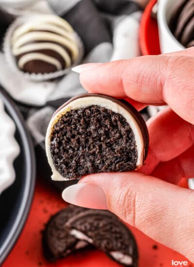 a hand holding an oreo truffle that has a bite taken out of it