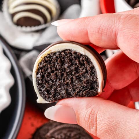 a hand holding an oreo truffle that has a bite taken out of it