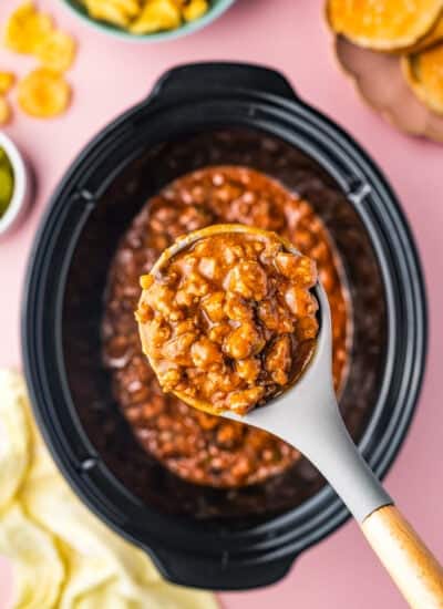 A crock pot full of sloppy joes with a spoon taking a serving out.