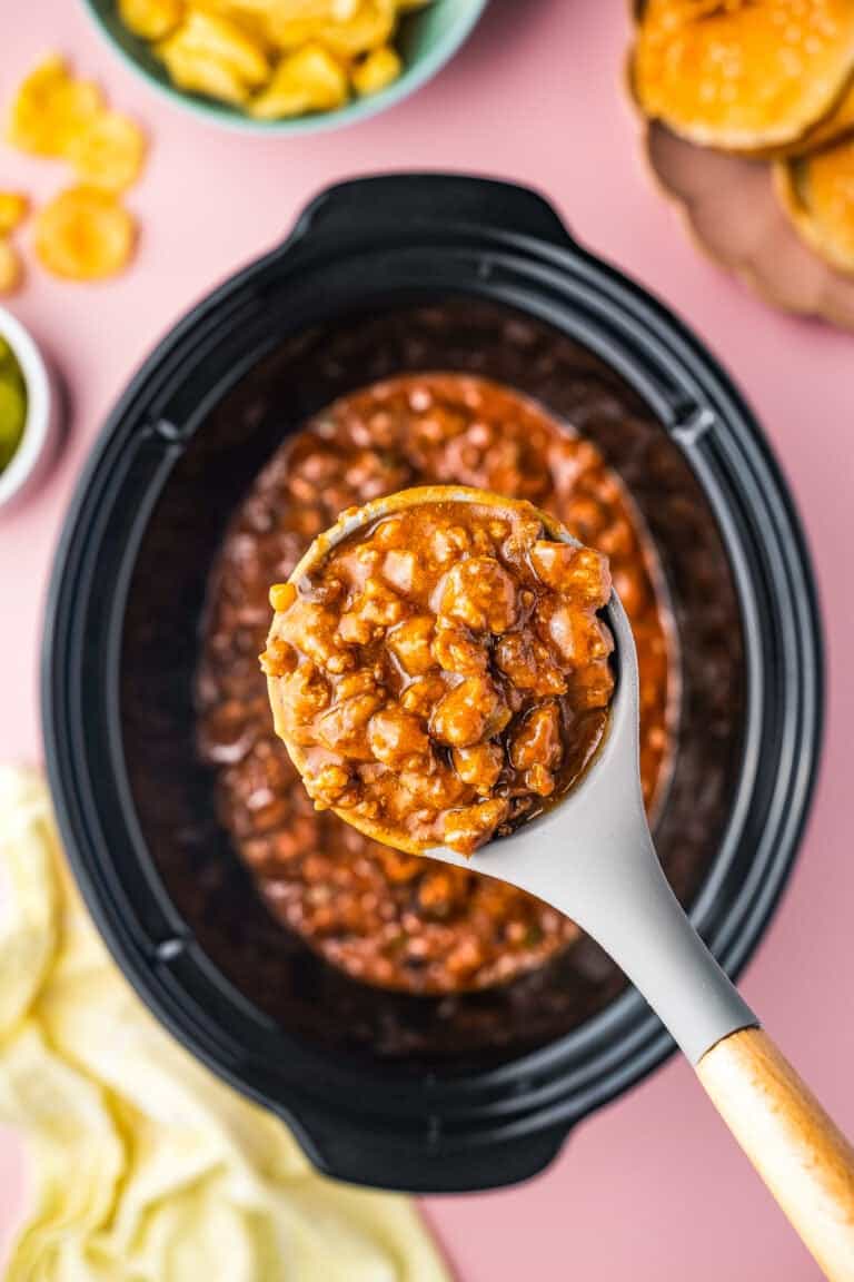 A crock pot full of sloppy joes with a spoon taking a serving out.