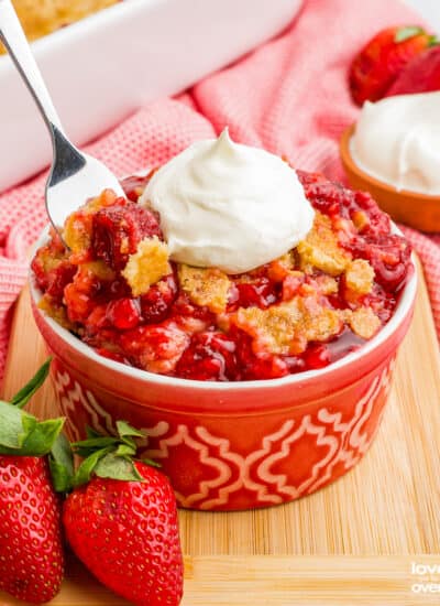 A spoon grabbing a portion of a strawberry dump cake topped with whipped cream.