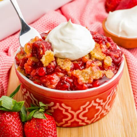 A spoon grabbing a portion of a strawberry dump cake topped with whipped cream.