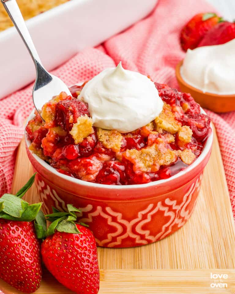 A spoon grabbing a portion of a strawberry dump cake topped with whipped cream.