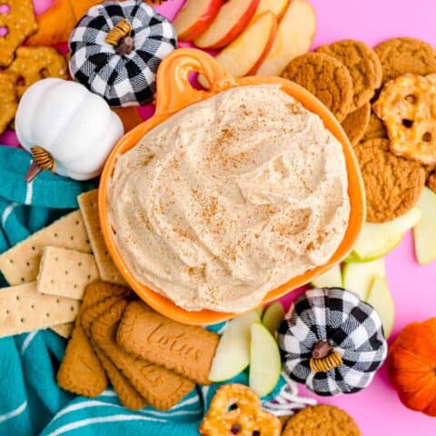 a pumpkin dish holding pumpkin dip, surrounded by cookies and pretzels