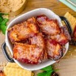 A bowl of candied bacon crackers with crackers and bacon sitting around it.